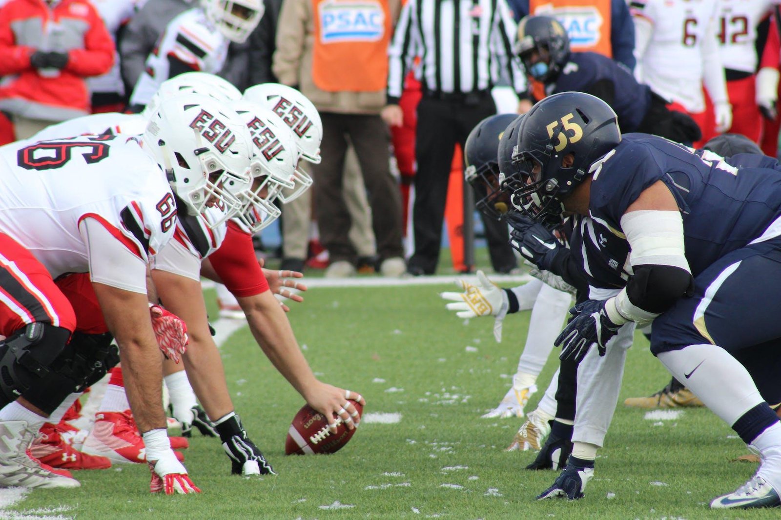 Two American football teams face off at the line of scrimmage on a grassy field, with one deploying a formidable seven man defensive line to disrupt their opponent's strategy.