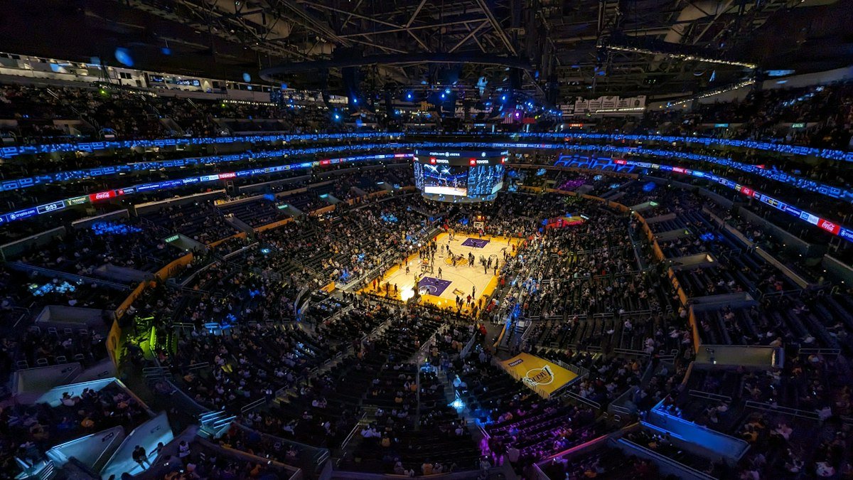 Basketball arena seen from the upper deck during a game, lit by blue arena lights