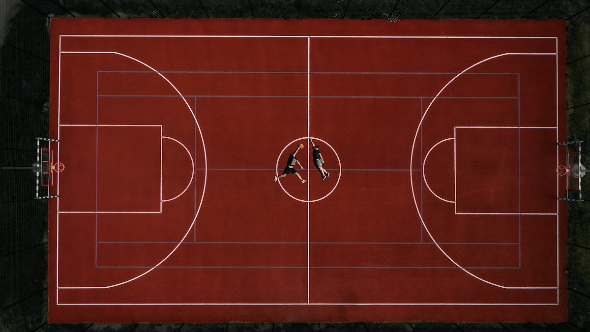 Aerial view of a red outdoor basketball court with two players lying at center court