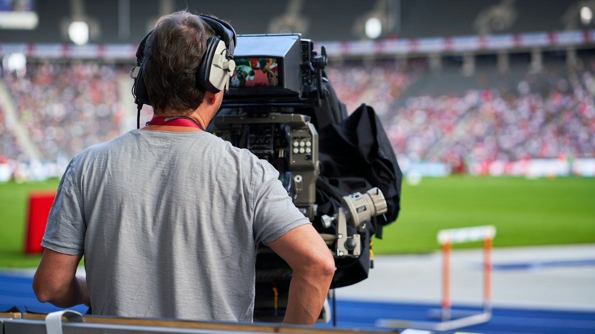 Camera operator wearing headphones at a stadium during a live sports broadcast
