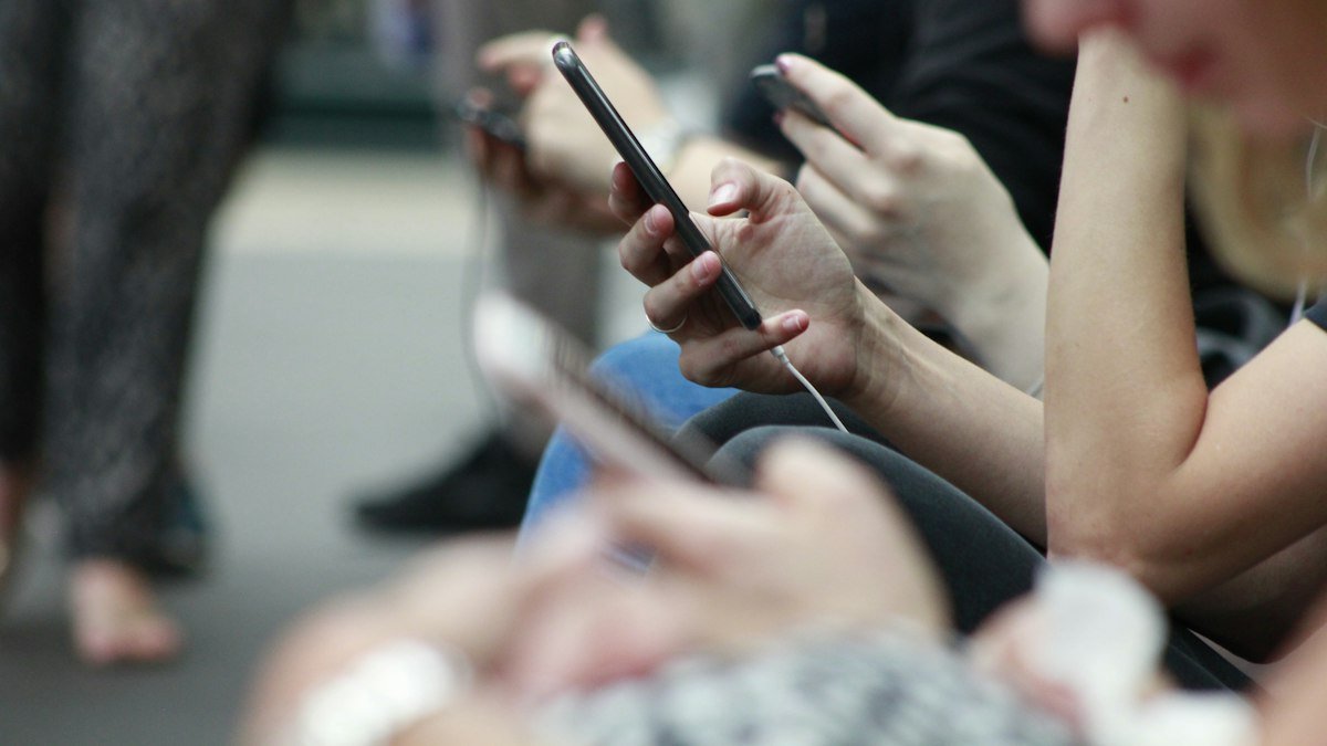 Hands holding smartphones as seated commuters scroll through their screens