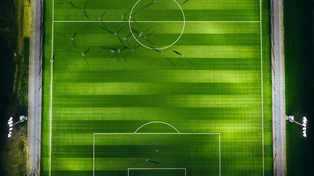Aerial view of a floodlit soccer pitch at night with players on the field