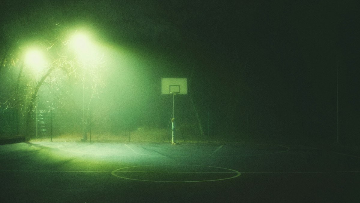 A basketball court lit by green floodlights in heavy fog at night