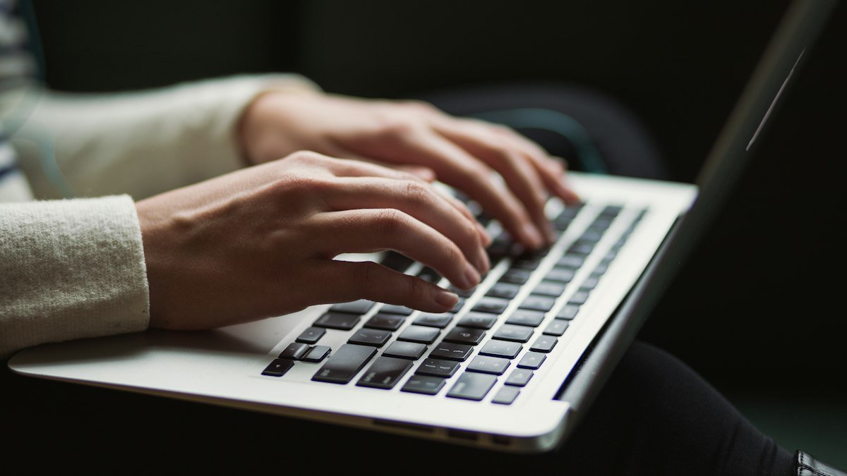 Close-up of a person's hands typing on a silver laptop keyboard