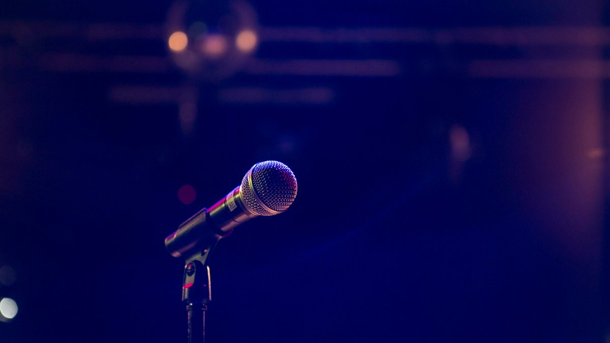 A microphone on a stand lit against a dark blue stage background