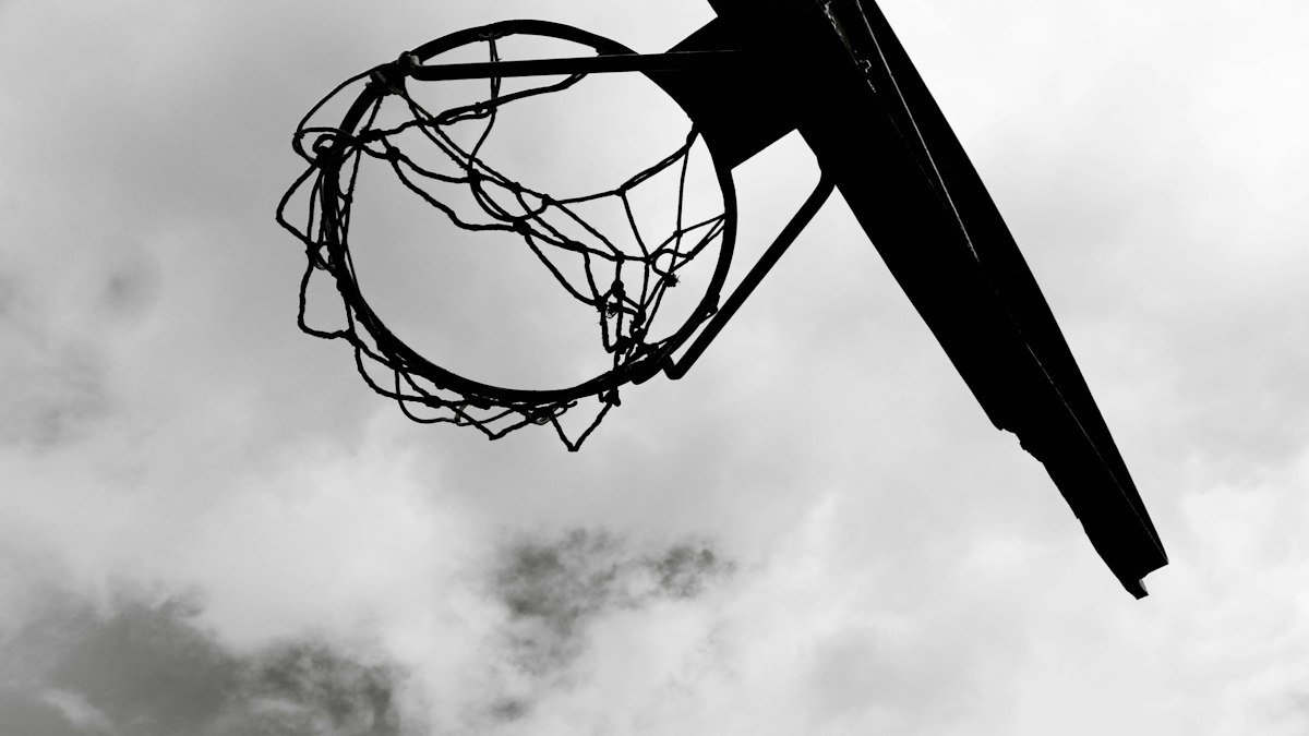 Black-and-white photo looking up at a basketball hoop, net and backboard against a cloudy sky
