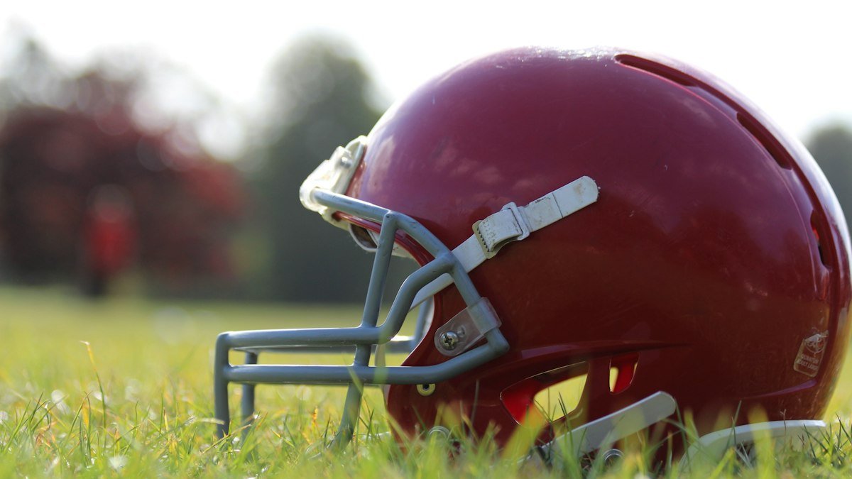 A red football helmet with a gray face mask resting on a grass field