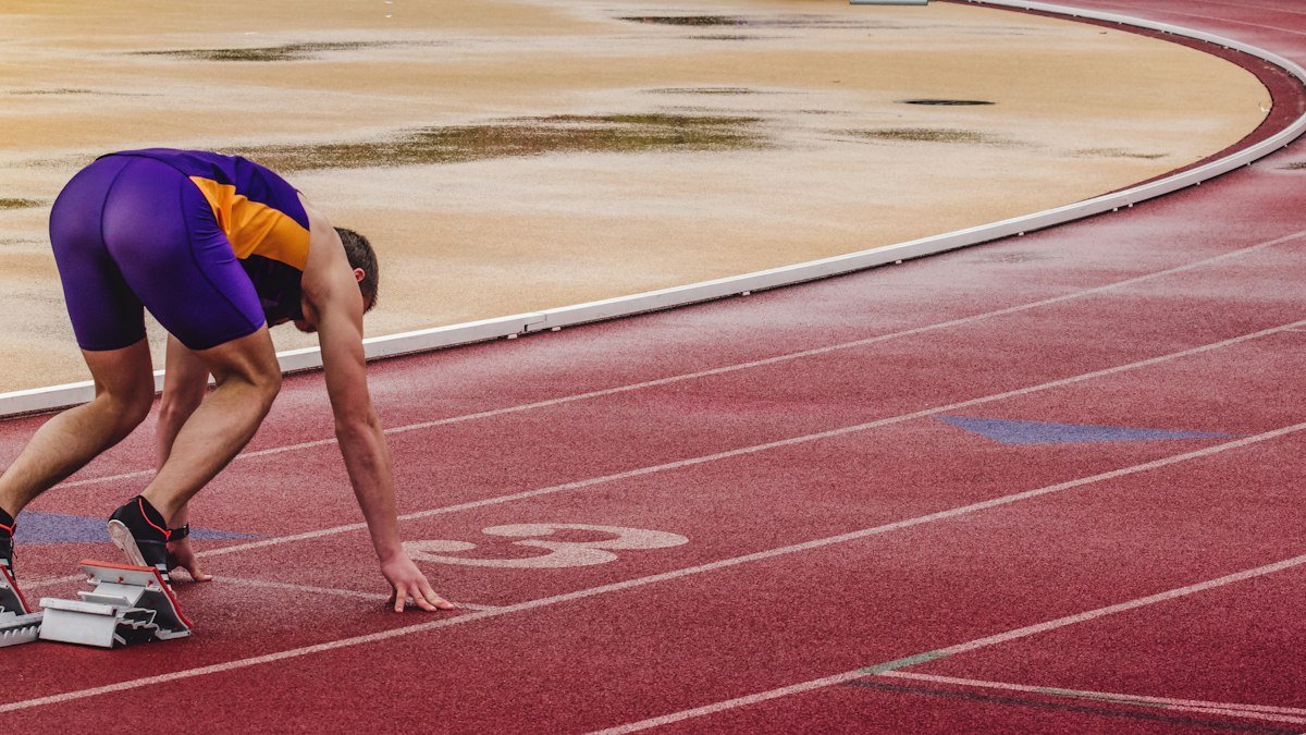 Sprinter crouched in the starting blocks on a red track before a race