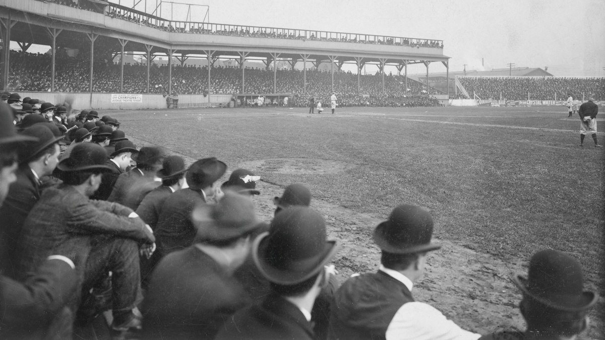 Crowd of men in bowler hats watching an early baseball game from the edge of a packed wooden ballpark, black-and-white archive photo