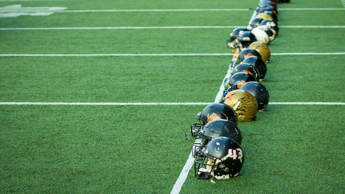 Row of black and gold football helmets lined up along a yard line on green turf