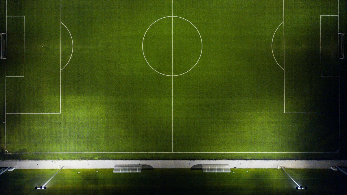 Overhead view of a floodlit soccer pitch with its markings and halfway circle.