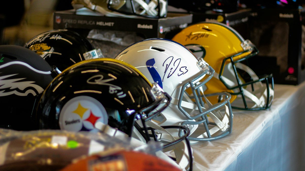 Row of signed NFL replica helmets on a display table, including Steelers, Colts and Packers designs