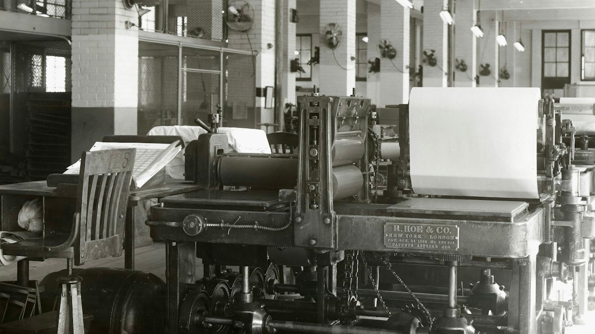 Black-and-white photograph of a vintage printing press in a factory